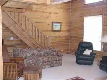 A portion of the Great Room, showing the log staircase to the huge loft. There are two sofas (one a sleeper) and the other is leather. Glider Rocker, and two overstuffed EZ chairs. 
Satellite TV.
Large picture windows looking out toward the forested lot complete the perfect picture!