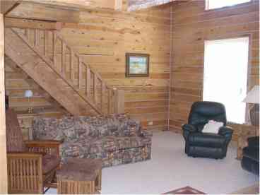 A portion of the Great Room, showing the log staircase to the huge loft. There are two sofas (one a sleeper) and the other is leather. Glider Rocker, and two overstuffed EZ chairs. 
Satellite TV.
Large picture windows looking out toward the forested lot complete the perfect picture!