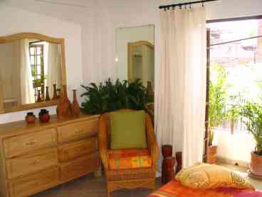 The overlarge Unit 2 front bedroom includes a queen sized bed, ample closet space, two large mirrors and a custom built dresser made from the local exotic wood, primivera. This photo shows the foot of the bed and our wrap-around balcony that is loaded with plants and has a nice view of our great neighborhood.