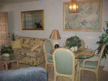 Living and Dining rooms. Lots of natural light. Entrance has fully screened porch. Faces East. Furniture includes entertainment center with TV, sofa and 2 chairs (one recliner), glass top dining, coffe and 2 end tables. Dining seats 4.