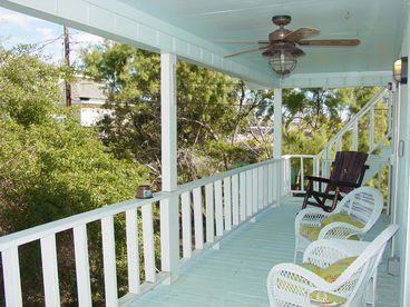 This is the back deck. It is always shaded and makes for a heckuva great spot to idle away the warm afternoons! It\'s accessible from each of the bedrooms. The steps lead up to the Captain\'s Walk on the roof and its spectacular views of Port Aransas. Please be careful on all decks and stairs: you\'ll be renting a pier-and-beam house and the first floor is already more than ten feet above the ground. Wicker chairs with comfy cushions and a convenient table await your rears and your beers at Deckhouse (but please do not take our chairs or towels to the beach). There\'s also a rustic rocker, an outdoor ceiling fan, and a couple of lighting options for you to enjoy. A few plastic chairs are scattered around Deckhouse so you can haul them up to the Walk, use them on one of the decks, or take them down to the grill/smoker (at the back of the carport) when it\'s time to scorch some meat.
