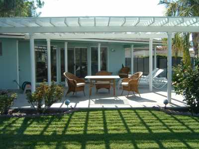 Backyard pergola and lawn area.  The wicker and glass patio set seats four.  There are two lounges and a side table.