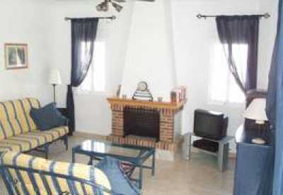 A large well presented room with open fireplace tastefully furnished with cane furniture.