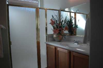 Sit-down bench featured in shower, bathroom has two sinks and vanity mirrors, with walk-in closet attached.