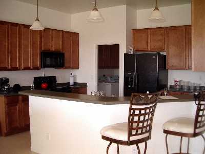 The fully furnished kitchen opens to the great room. It includes microwave, dishwasher, stove and Corian countertops. It connects to the utility room with washer and dryer, and then into the 2 car garage with door opener.