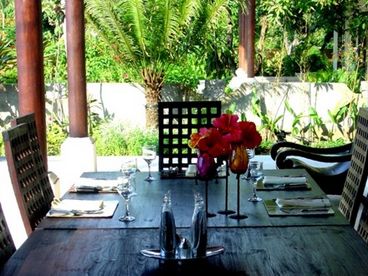 Dining area on the terrace by the pool with a backdrop of gardens.