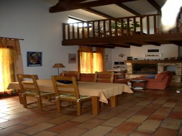 This view of the dining area (foreground) with the living room with wood-burning fireplace behind and the loft above.