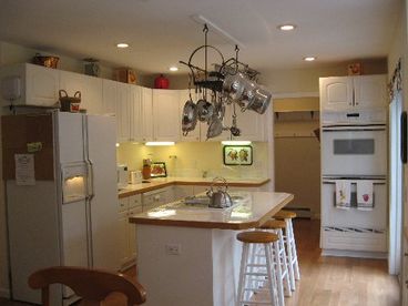 The Kitchen features a Center Island with Glass Cook Top and Breakfast Bar as well as a Double Convection Oven, Side by Side Refrigerator and a Lovely Wrought Iron Pot Rack with New Stainless Steel Cookware.