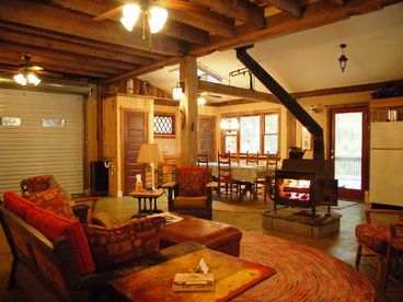 The ground floor living area, dining, kitchen and entertainment space. A large overhead door opens to reveal a concrete patio and the forest behind it.