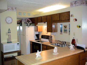 The spacious kitchen is open to the living and dining spaces, creating one large great room. The kitchen is fully equipped with everything you need to create delicious meals, including microwave, oven and range, full-size refrigerator, toaster, electric can opener, glass blender, programmable coffee maker, electric can opener, hand mixer, and non stick pots and pats. The dining area, which is just on the other side of the counter, features a table with four chairs. 
