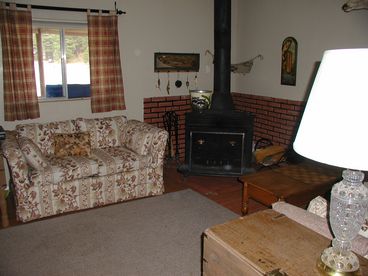 View of left side of living room and wood burning fire place. Whole cabin has wood floors and blinds on all windows. 