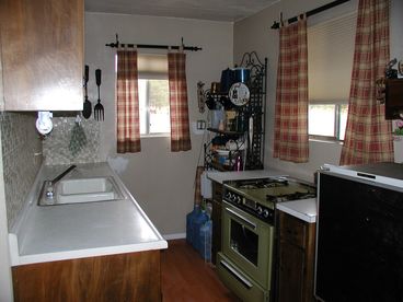Kitchen, stove with oven small camping refrigerator. Pots, pans, dishes, silverware.  