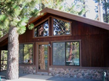 Donner Lake Vacation Rental with tree growing through the deck, providing shade and character. The large deck has table, chairs and umbrella. Plus lawn furniture.