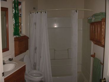 Roomy Bathroom has full tub with shower, sink with vanity, cabinets on two walls, mirror and window.
