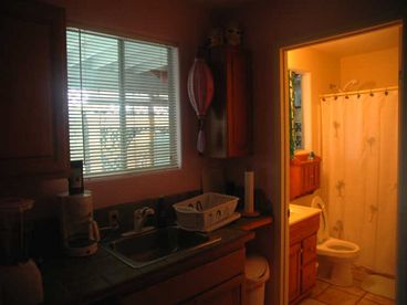 Kitchenette with full size sink and cabinets and window; Private bathroom has full sized tub and shower, sink with cabinet and window.