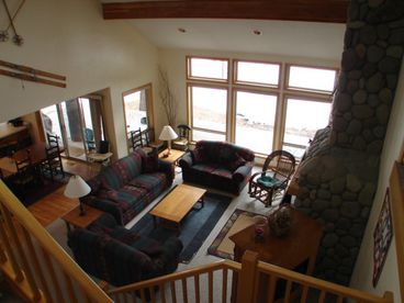 Two story great room has exposed wood beams and a wood burning river rock fireplace.