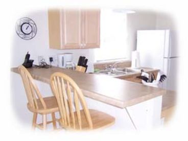 Kitchen area is fully equipped, has a countertop with two bar stools