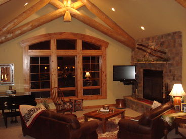 Lodge great room with log trusses and extra-large woodburning fireplace.  Note the Baby Grand piano on the far left.