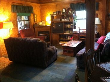 Open concept cabin has large living area with sofa, loveseat, recliner, fireplace, entertainment center, desk.