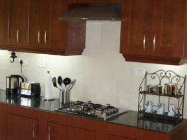Well equipped kitchen features a four burner hob with chimney, granite counter top, cookware, tableware, cutlery, microwave, fridge, toaster.