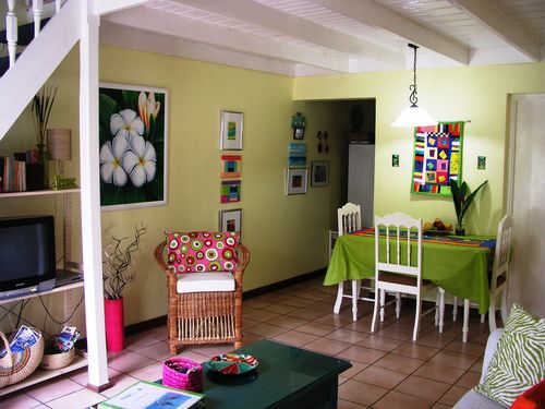 The living and dining area looks out onto the balcony, which overlooks the pool and private beach. The bathroom is the door at the right with hot water and colorful artwork on display.