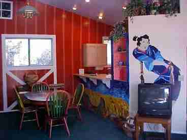 This is a view from the livingroom with cathedral ceilings and unique wall art which includes a replication of a van gogh painting and faux barn wall. An angel is stained onto the dining room table with matching chairs.