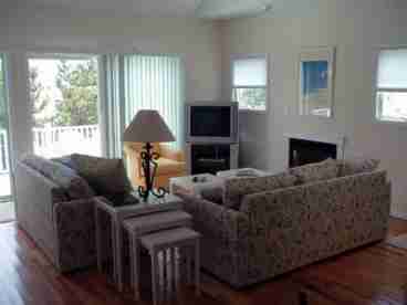 Sun-drenched living room with gas fireplace, hardwood floors and double sliders opening to a large deck. 