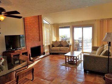 Looking out from the kitchen, dining table with ceiling fan, cable tv, and living room seating. All is looking out at the ocean front, and patio