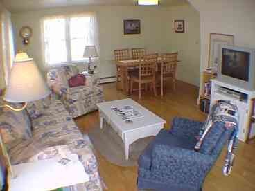 Sun-filled, comfortable living room, dining room with large table and 6 chairs. Lace curtains invite the coastal light in, and the many windows allow fresh ocean breezes to waft through, lifting the curtains in a gentle dance. 
Relax with new flatscreen TV (bought since this photo was taken) and a collection of area guides, paperback fiction and seating for 6.  Out of view is the fully equipped kitchen (dishwasher, electric stove, microwave, coffee maker, blender, wine glasses, etc. Everything you\'ll need to make this your home during your vacation in Maine\'s Acadia National Park region!